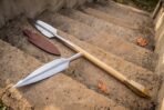 Spear with leaf shaped steel head and brass butt spike on sandstone steps, a second loose head and leather sheath beside it