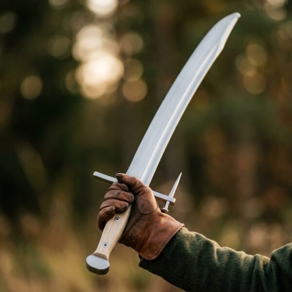 Spring steel langes messer with curved single edged blade held aloft in a leather gloved hand against a forest