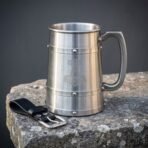 Stainless steel Viking tankard with etched hammer and three riveted bands on a stone block beside a black leather hanger with buckle