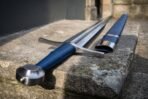 Steel arming sword with blue leather grip and round pommel beside its blue scabbard, close up on a stone ledge