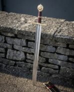 Steel arming sword with a brass wheel pommel, brass crossguard and oxblood leather grip leaning on a dry stone wall