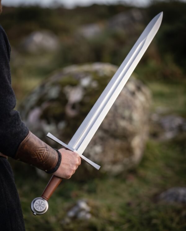 Steel arming sword with fullered blade, straight cross and Vegvisir disc pommel held in hand on open moorland