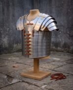 Steel banded Roman cuirass with brass fittings and leather straps on a wooden stand, spare strap on the paving