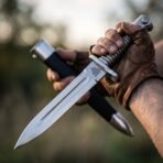 Steel bayonet with ribbed grip, Valknut etching and fullered spear point blade held beside its black scabbard
