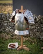 Steel cuirass with laminated pauldrons, roped edges and tan leather straps on a wooden stand, three quarter view against a dry stone wall