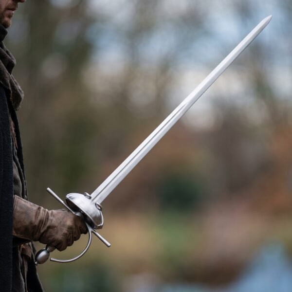 Steel dished shell rapier trainer held in a gloved hand with the long narrow blade angled up outdoors