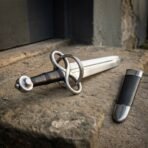 Steel fantasy sword with loop guard lying on a stone ledge next to its black leather scabbard with steel chape