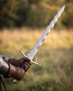 Steel flamberge sword with a wavy flame blade and brass ring guard held in gloved hands, leather grip, golden meadow behind