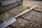 Steel glaive head with a hooked spine and knotwork engraving on an ash haft with steel langets, laid on paving stones