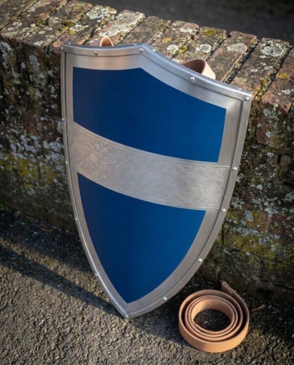 Steel heater shield with blue painted face and engraved Celtic knot band leaning on a brick wall beside a leather strap