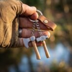 Steel keyring with miniature axe and valknut hammer dangling from a hand in front of a blurred river bank