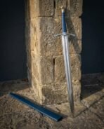 Steel knightly sword with blue leather grip and runes cut above the guard leaning on a sandstone pillar beside a blue scabbard