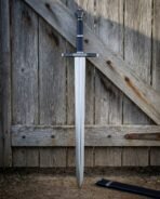 Steel longsword with black faceted pommel and straight cross standing point down against a braced wooden door