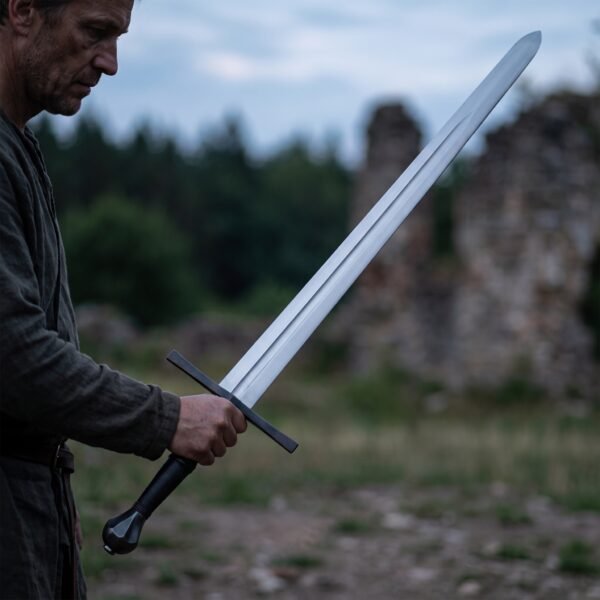 Steel longsword with blackened cross held low across the body by a man in front of ruined walls