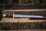 Steel medieval sword with brass hilt and oxblood leather grip lying on stone steps beside its oxblood scabbard