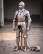 Steel plate armour suit with close helm on a wooden stand, padded arming kit and spare straps on the paving