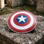 Steel round shield replica painted in concentric red and white bands with a white five pointed star on a blue centre disc, resting on weathered stone