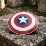 Steel round shield replica painted in concentric red and white bands with a white five pointed star on a blue centre disc, resting on weathered stone