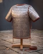 Steel scale armour shirt with overlapping riveted scales and russet leather binding, standing on a wooden stand in a flagstone yard