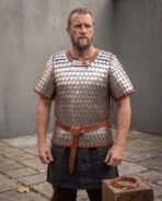 Steel scale armour shirt with russet leather edging worn by a bearded man with a brown leather belt, standing in a stone courtyard
