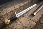 Steel short sword with brass lion head pommel, brass guard and knotwork etched fuller lying on a sandstone wall beside its scabbard