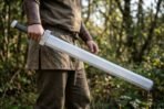 Steel sword with knotwork engraved guard, block pommel and dark grip carried at the hip by a man in a brown tunic in woodland