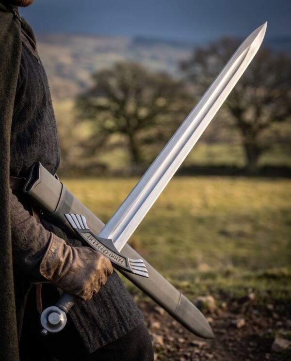 Steel sword with ring pommel drawn from its black scabbard by a gloved hand in a brown cloak, open fields behind