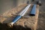 Steel sword with blue leather grip, curved steel guard and faceted brass pommel lying on a stone step by a blue scabbard