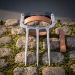 Steel three blade knuckle claw with riveted frame, knotwork cut black knuckle plate and tan leather hand strap on mossy cobbles