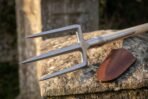 Steel three prong trident head with knurled collar on an ash haft resting on a stone gate pillar beside a leather sheath