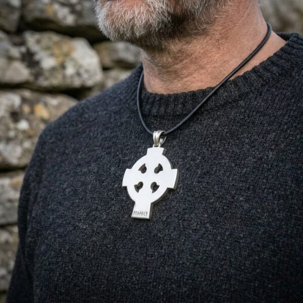 Steel tone Celtic cross pendant on a black leather cord worn over a charcoal wool jumper by a bearded man