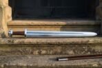 Steel Viking sword with a full rune row on the blade laid flat along a stone step, brown leather scabbard with steel chape on the step below