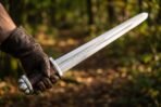 Steel Viking sword with a lobed pommel and rune engraved blade held out in a gloved hand against autumn woodland