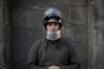 Steel visored helmet with a riveted brow band and perforated bevor worn with a chainmail coif by a man in a grey tunic