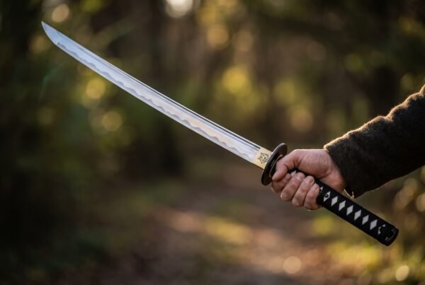 Steel wakizashi short sword with a wavy hamon, black ito wrapped tsuka and brass habaki held out in a hand on a forest track
