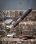 Steel war hammer with walnut haft and black leather wrap resting on brick steps above its brown leather head cover