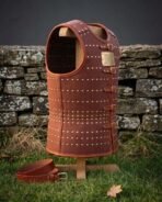 Studded russet leather cuirass on a wooden stand in front of a dry stone wall with a matching leather belt on the grass