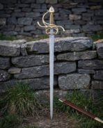Swept hilt sword upright against a grey dry stone wall with its brown leather scabbard in the grass, layered Damascus pattern flowing the length of the slender blade