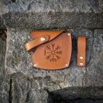 Tan leather axe sheath with Vegvisir stamp, brass snaps and a separate belt loop laid flat on grey stone