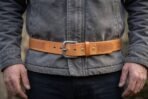 Tan leather belt with stamped Celtic knotwork panel and antiqued buckle worn over a grey jacket