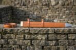 Tan leather sword scabbard with tooled runes and steel chape laid on a dry stone wall beside a matching belt