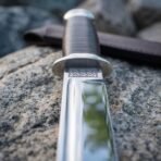 Tanto knife with knotwork engraved steel guard and stacked leather grip, close up of the guard and fullered blade on granite
