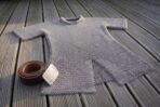 Thigh length butted steel chainmail hauberk with short sleeves and split skirt laid on wooden decking, coiled brown belt with a knotwork buckle