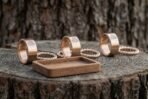 Three bronze tone valknut stamped bands and three twisted wire rings on a sawn tree stump with a small walnut tray in front