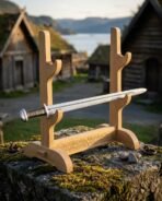 Three tier oak sword display stand with knotwork engraved crossbar holding a sword on a mossy wall in front of turf roofed houses