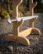 Close up of a three tier oak sword stand with knotwork engraved crossbar and footed base, sword hilt resting in the top cradle