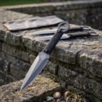 Throwing knife set with paracord wrapped grips and ring ends laid on a dry stone wall beside a leather roll