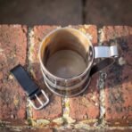 Top down view into a horn tankard with steel bands and handle on lichen covered bricks next to a black leather belt loop