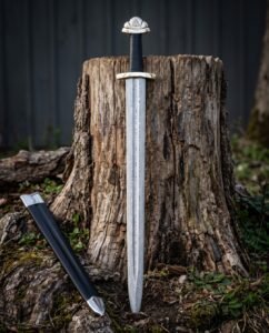 Triquetra damascus sword with a pattern welded Viking blade, three lobed pommel and black leather grip standing against a weathered tree stump