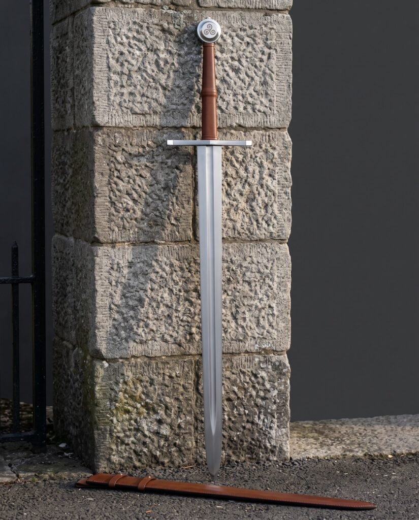 Triskele sword with a triple spiral wheel pommel and tan leather grip standing against a granite gatepost above its tooled tan leather scabbard with belt loops